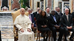 A group of people in suits sit with the Pope in chairs