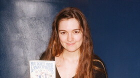 A woman with long brown hair holds a copy of the book "You Don't Need a Smartphone." Several copies of the book are splayed out on a table in front of her. 