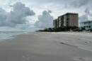 A tan high rise alongside a beach with light grey, cloudy skies