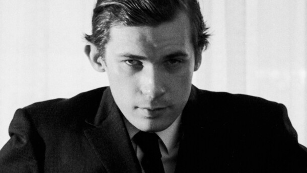 pianist Glenn Gould in his younger years, in a coat and tie, staring at the camera