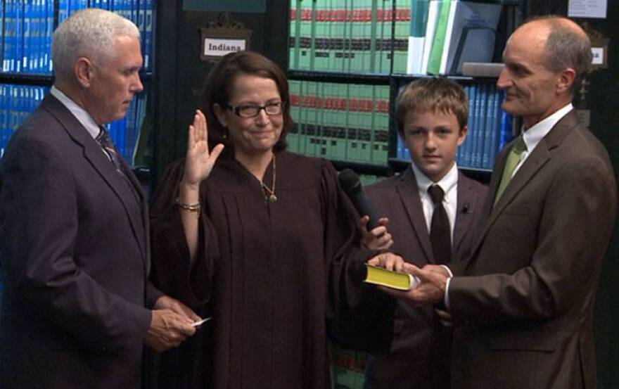 Gov. Mike Pence swears in Loretta Rush as Chief Justice of the Indiana Supreme Court, as her son Luke and husband Jim, look on.