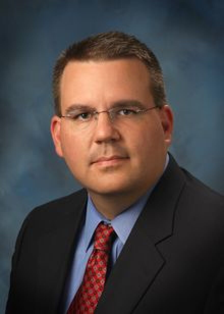 Closeup of man in a dark suit with a blue shirt, red tie and glasses