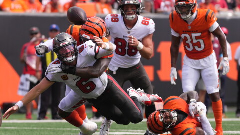 football player in white jersey and pewter helmet is tackled and watches the ball leaves his hands and is in the air. behind him is another player who made the tackle in an orange jersey and helmet on the ground, and two other players running from behind them