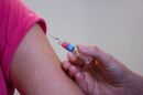 a person's upper arm with part of their sleeve visible, and a hand holding a syringe near the arm