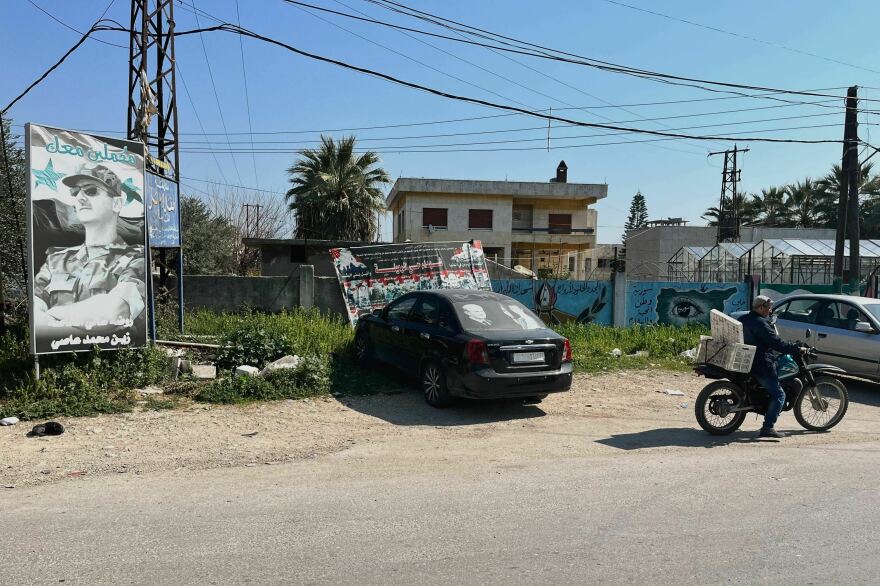 تظهر هذه الصورة ملصق الرئيس السوري تحت الشعار "نواصل معك" بجانب صور جنود قتلوا في معركة في مدينة جبالة. وتوجد على نافذة السيارة صور الرئيس ووالده حافظ الأسد الذي حكم سوريا حتى وفاته عام 2000.