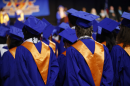The backs of a crowd of graduates in blue graduation gowns wearing gold sashes