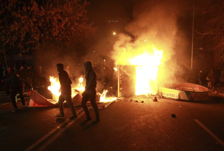 People walk past a burning public booth during student demonstrations in Santiago, Chile.