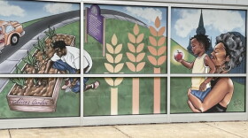 A mural on the outside of the Feeding America Eastern Wisconsin building in Milwaukee depicts a scene of a man tending to crops at the nearby Alice's Garden, and a woman carrying a child who's holding an apple