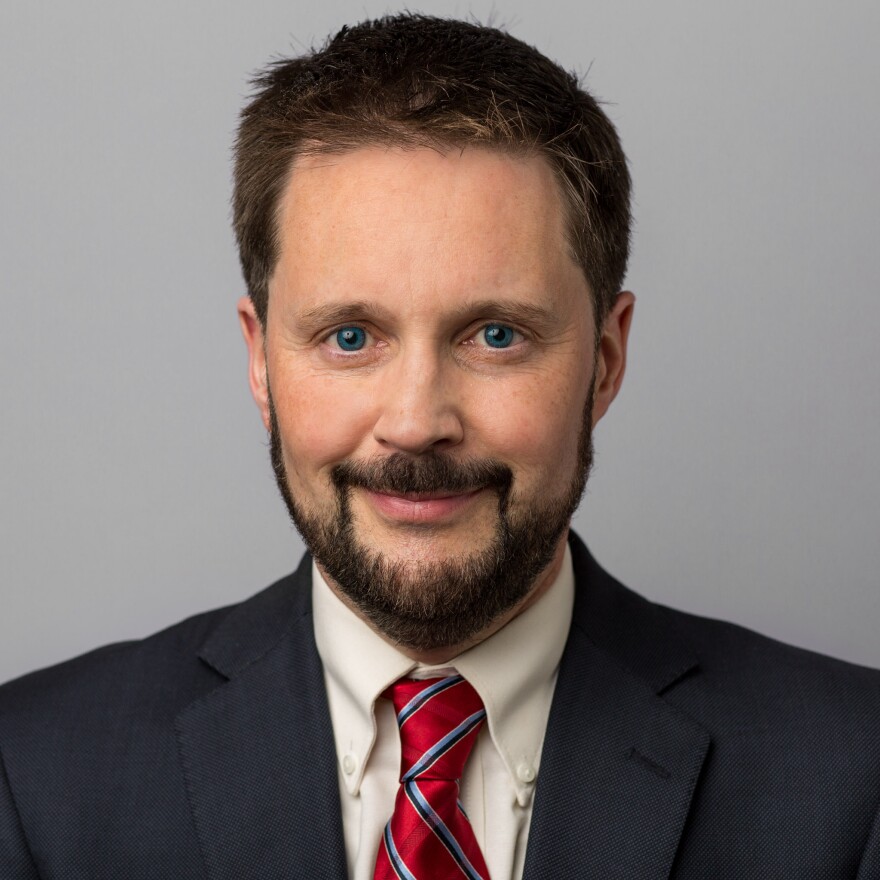 Pete Sepp stands in front of a grey background. 