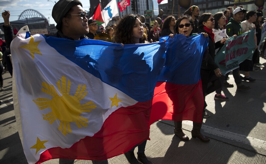 From left, Aaron Verzosa, Amber Manuguio and Emma Catague carry the national flag of the Philippines during the annual March for Immigrant and Workers Rights on Tuesday, May 1, 2018, in Seattle.