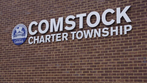 On a brick wall, a sign reads "Comstock Charter Township" and is depicted with the township seal next to it. 