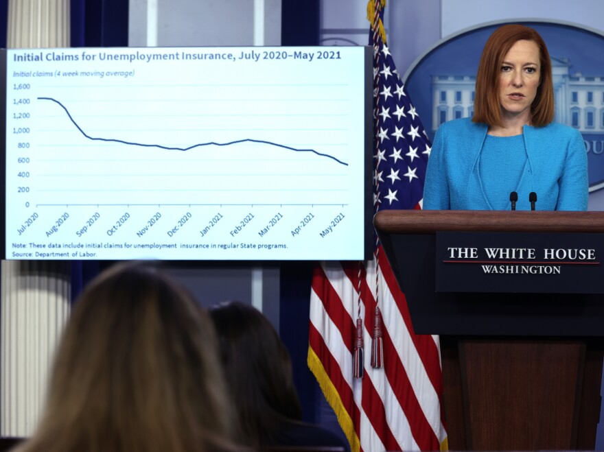 White House press secretary Jen Psaki addresses a news briefing last month as a chart showing a drop in initial claims for unemployment insurance appears on a monitor.