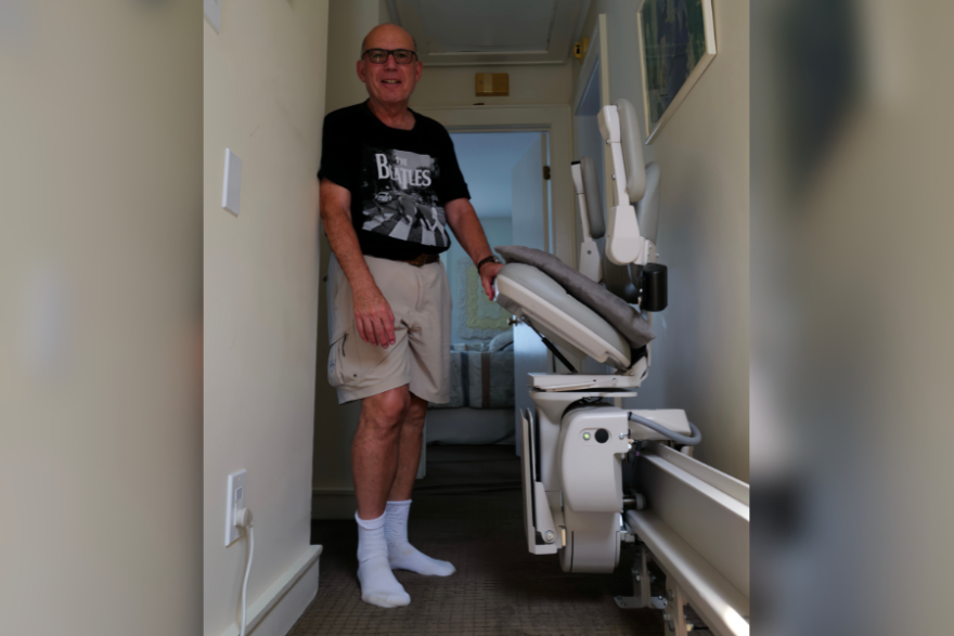 Howard Weinberg, a retired physician living with Parkinson’s disease, stands beside a stair lift at his Virginia Beach home.