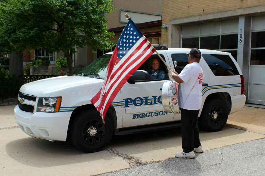 A man with an American flag stands in front of a Ferguson Police car earlier in July. A wide-ranging municipal court bill that takes effect on Friday doesn't impact Ferguson as much as other cities in the St. Louis region. 2015