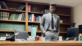 A person in a suit stands behind a desk