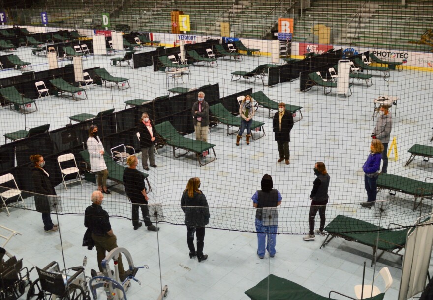 People standing between cots in a hockey arena.