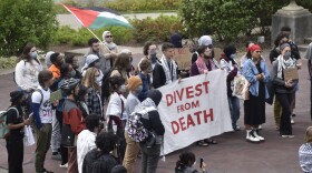 Protestors gather at Mirror Lake on Ohio State University's campus. They hold a sign that says "Divest from Death" and fly Palestinian flags.