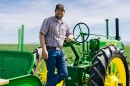 Colby Frey leans on a green John Deere tractor.