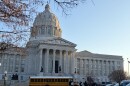 A yellow school bus is pulled up in front of the Missouri State capitol building. 