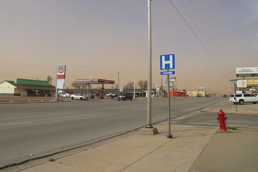 Photo of a road sign indicating the direction of a hospital. There is a dust storm in the distance.