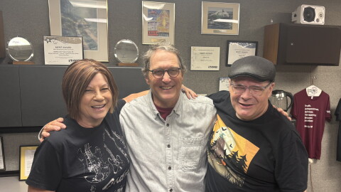 Linda Smith, B.G. Bradley, and Marty Achatz stand arm in arm and smile just outside of Public Radio 90’s Studio A.