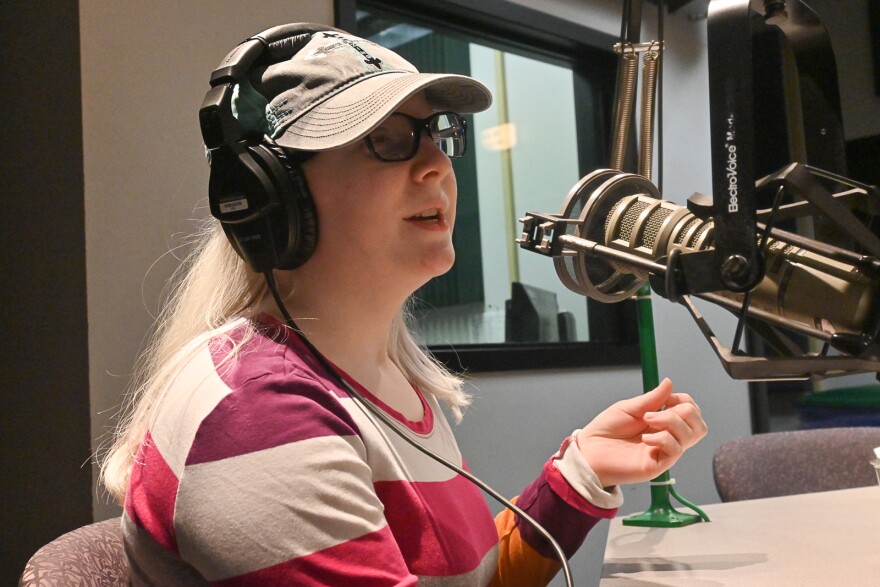 Woman wearing a cap and striped shirt gestures and talks at a microphone