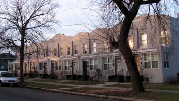 A long row of two-story concrete historic terrace townhomes under a evening sky, lined with bare winter trees and a street in the foreground.
