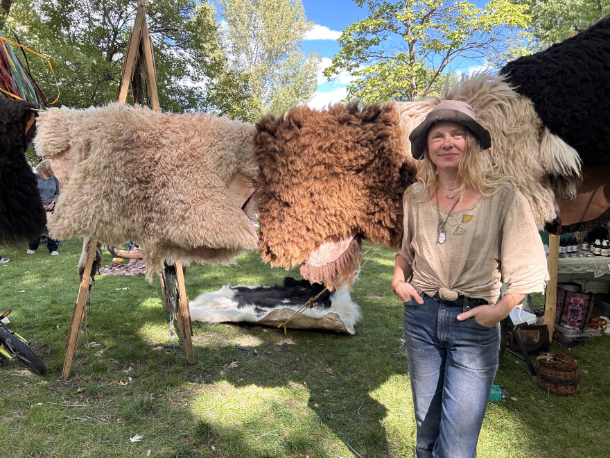 A rtist Kelly Moody at the Mountain Harvest Festival standing in front of hides tanned.