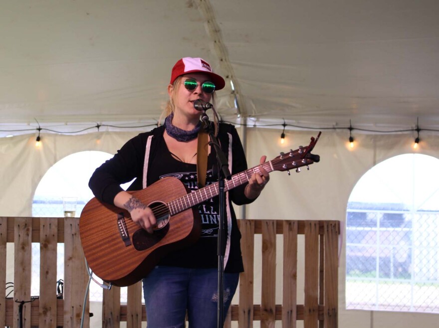 Woman in a trucker hat playing guitar and singing into a microphone