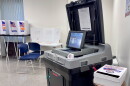 A gray voting machine sits open, with guarded places for voters to cast their ballots behind the machine.