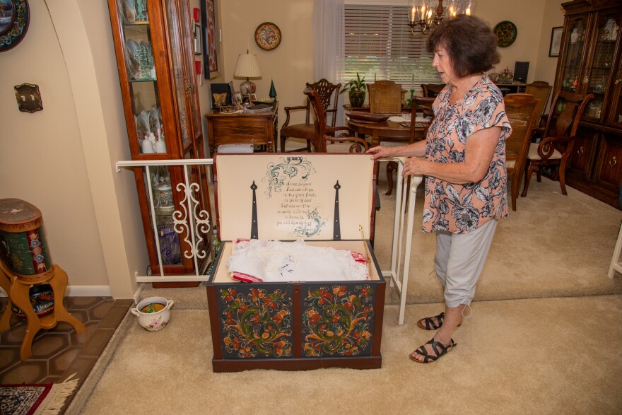 A woman stands next to a painted trunk with the lid open. 