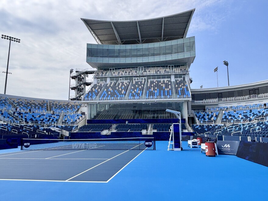 An empty blue tennis court surrounded by hundreds of vaulted seats