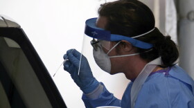 Stephen Bonett, a nurse and Philadelphia Medical Reserve Corps volunteer, administers a nasal swab to a driver at the city's coronavirus testing site next to Citizens Bank Park in South Philadelphia on Friday, March 20, 2020. The site, which opened Friday afternoon, is the first city-run drive-through location where people can be swabbed to determine if they have the coronavirus. At the time of opening, it was only for people with symptoms who are over 50 and healthcare workers with symptoms. (Tim Tai/The Philadelphia Inquirer via AP)