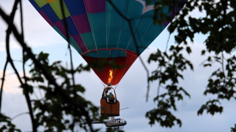 A balloon called the Fleckfolly 5 soared overhead while passengers in a helicopter ride look on at the Suncook Valley Rotary's 44th annual hot air balloon rally on Friday July 31, 2026.
