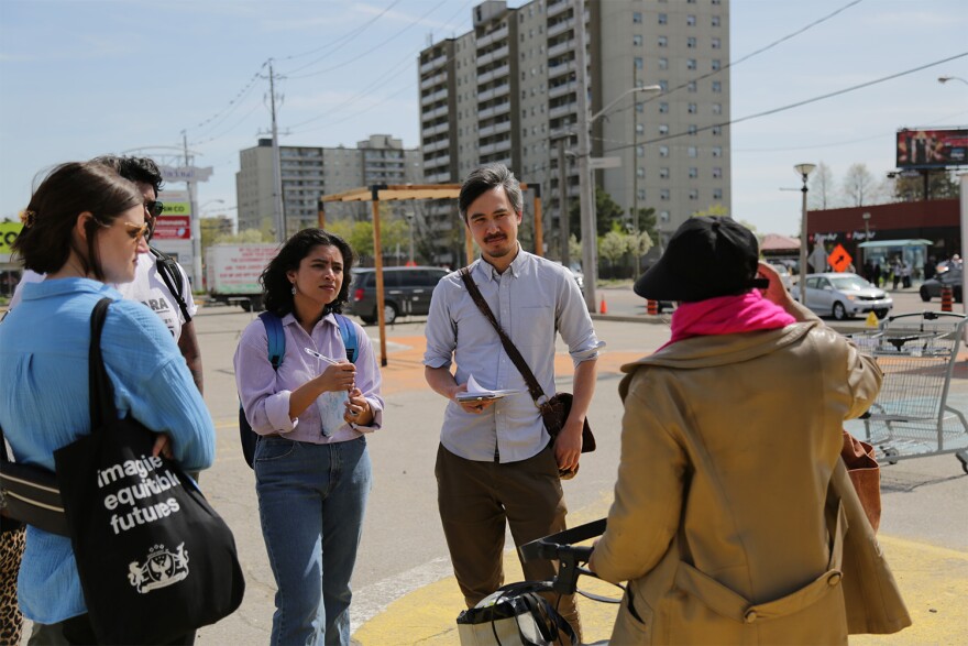 Nicholas Hune-Brown (pictured center right) is talking with a group of four people on a sidewalk near an intersection. 