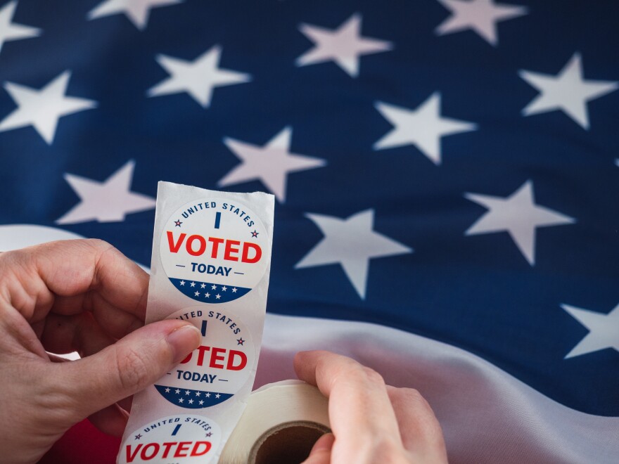 Woman's hand holding stickers that says: " I voted ". background with usa flag