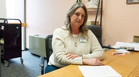 A woman in a white sweater looks at the camera while sitting behind a desk