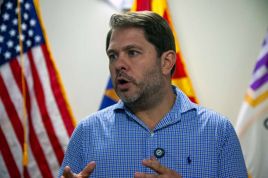 Gallego talking in front of flags
