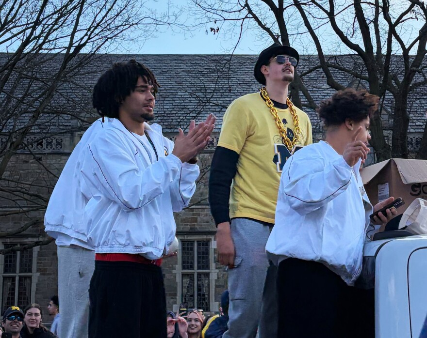 Basketball players Elliot Cadeau (left), Aday Mara (middle), and Howard Eisley Jr. (right) at the parade, riding in a white vehicle.