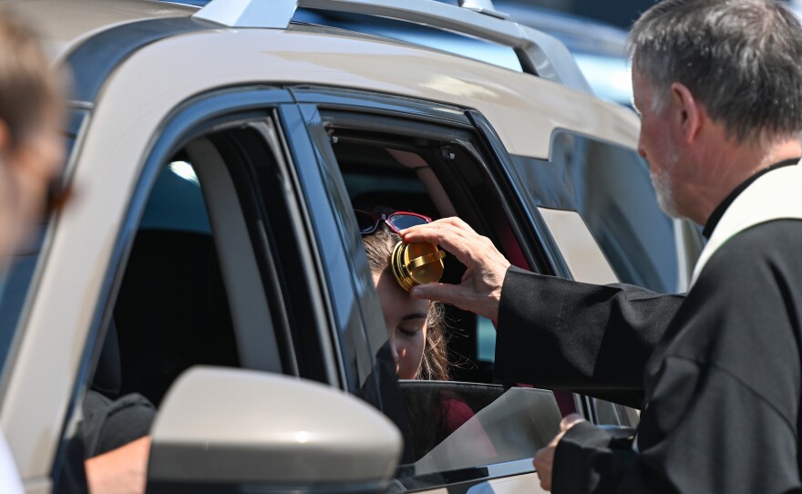 father Paul Fagan blesses and gives communion to those in cars during the St Ann's Novena Monday.
