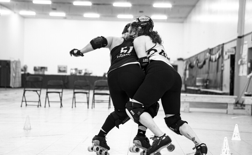 Two women skate on a roller derby rink.