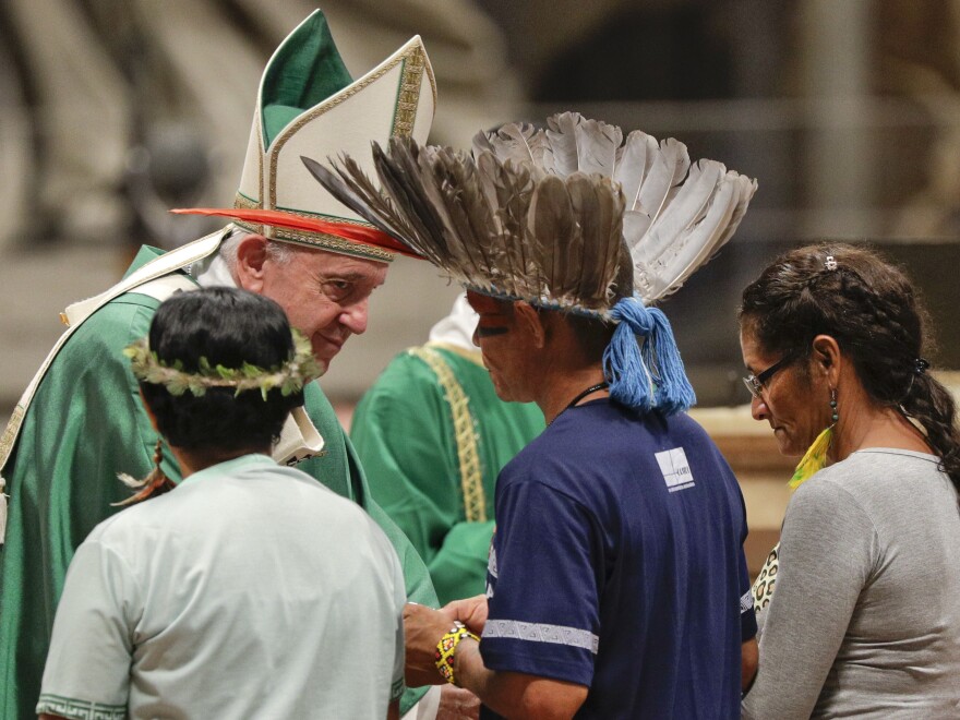 Indigenous peoples, some with their faces painted and wearing feathered headdresses, stand by Pope Francis as he celebrates an opening Mass for the Amazon synod on Sunday.