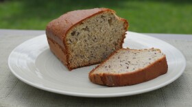 A loaf of banana bread with a slice cut off of it on a white plate