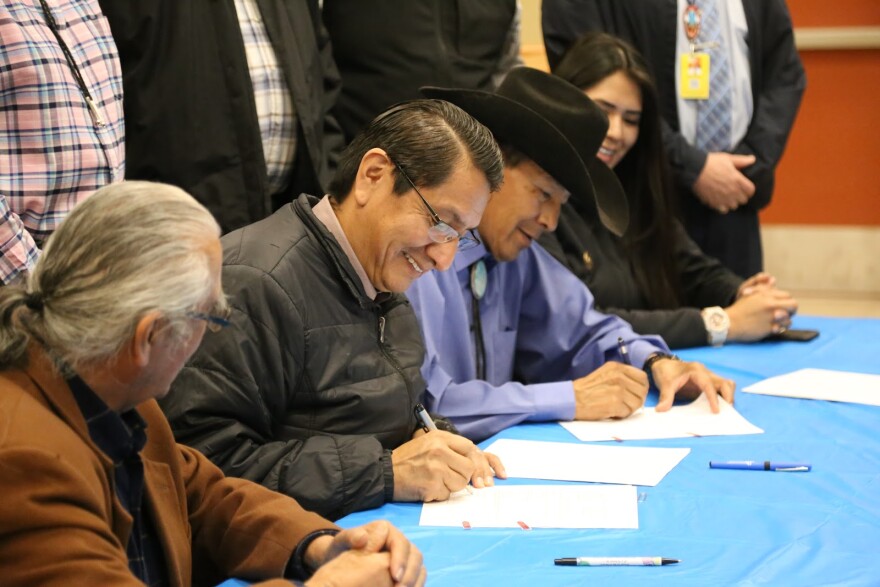 Photo of three men and a woman sitting at a table smiling and signing papers