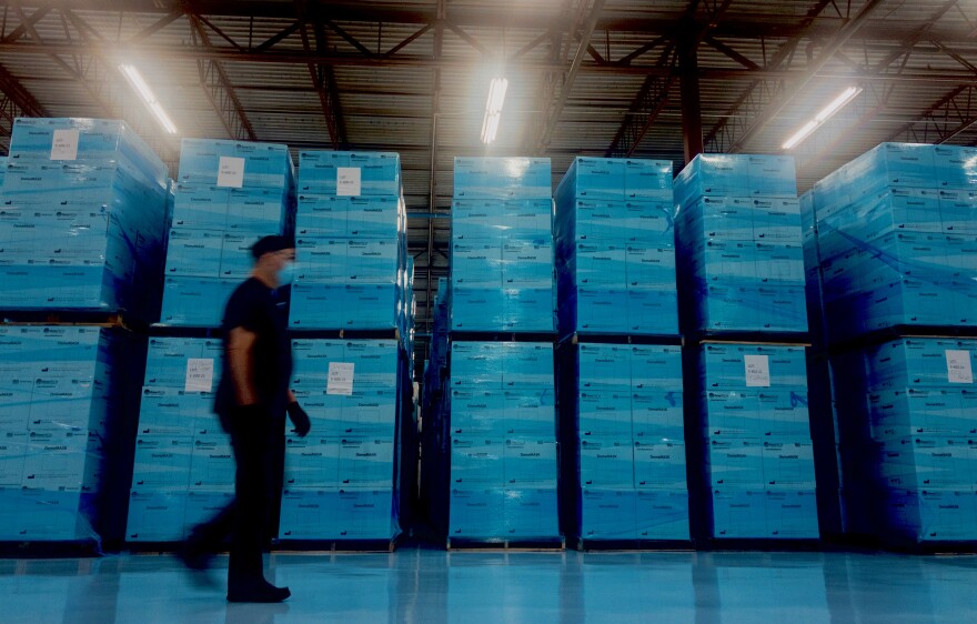 A worker walks past pallets of surgical masks in a warehouse