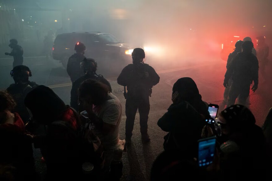 Protestors cover their eyes and ears as agents look on.