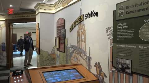 A painted wall says, "Citizen station," with panels about the three branches of government. In the foreground is an interactive display and corded telephone.
