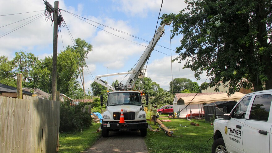 A large truck with an arm begins to lift a power pole in a back alley. 