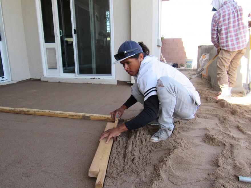 Raul Torres uses a piece of wood to level the ground for a new patio.