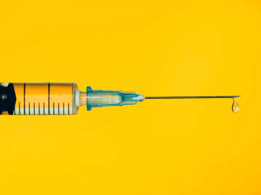 Closeup contemporary disposable syringe with drop of fluid medication on needle placed against vivid yellow background. Vaccination is the most anticipated procedure of the year. Research of coronavirus disease protection concept. Covid-19 vaccine studies.